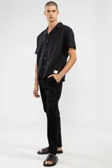 Camisa negra de manga corta con cuello camp y calce relajado. Confeccionada en mezcla de algodón y lino con botones de coco con logo y parche característico de Polonio.