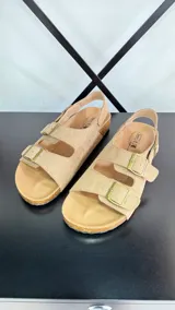 Sandalias planas color marrón claro con dos tiras anchas con hebillas y tira trasera.