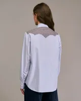 Camisa de manga larga con cuello abotonado, de corte recto, con canesú y puños a cuadros. El cuerpo de la camisa es a rayas verticales celestes y blancas.