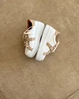 Zapatillas deportivas urbanas con capellada negra, detalles en beige y suela blanca.