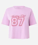 Remera corta de manga corta color rosa claro, con cuello redondo y estampado frontal que incluye el texto "Sporting Club" y el número "87" en rojo.