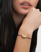 Pulsera PD Paola con cordón negro y dije dorado en forma de flecha.