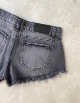 Short de jean negro con efecto acid wash, tiro bajo, con roturas y terminación deshilachada en el ruedo. Presenta detalles de ojales metálicos y tiras de ajuste laterales.