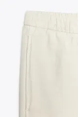 Pantalón culotte color crudo, de tiro medio, cintura elástica ajustable con cordones y bolsillos laterales ocultos en la costura.