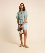 Blusa de tricolina a rayas verticales blancas y verdes, con cuello redondo, mangas cortas abullonadas y lazos delanteros.