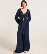 Blusa de mangas largas color azul marino, confeccionada en viscolino con 30% de lino, con escote V, lazo en el cuello con punta y bieses contrastantes luego abajo del escote, además del bajo de volado.