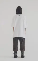 Remera blanca de algodón con cuello redondo y calce oversize. Estampa frontal con diseño de planta de cannabis, texto "Neurobotánica" y patrón geométrico.