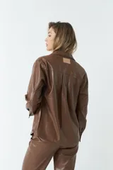 Sobrecamisa color beige de efecto cuero, con cuello clásico, cierre frontal con botones a tono, mangas largas con puños abotonados, dos bolsillos con solapa en el pecho y corte recto.