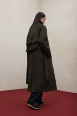 Abrigo largo confeccionado en lana reciclada de color verde oscuro, con cuello alto, mangas raglán y cinturón ajustable a tono. Presenta un diseño de corte holgado y elegante ideal para climas fríos.
