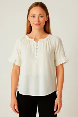 Blusa color blanco de lino y viscosa, con cuello a la base, mangas cortas con volados y cierre frontal con botones.
