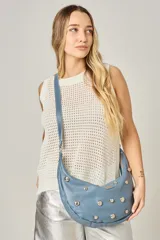 Cartera tipo bandolera de cuero sintético color celeste, con forma de media luna y tachas metálicas redondas plateadas en el frente. Posee correa ajustable y placa metálica con logo en la parte superior.
