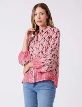 Camisa de gasa con cuello con solapa y apertura central con botones. Presenta un estampado de patrones geométricos en tonos rosados, marrones y crema, con un borde inferior en un patrón geométrico más denso en tonos rojizos/rosados. Las mangas son amplias de largo tres cuartos con puño elastizado.