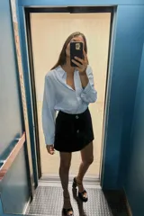Camisa marrón de corte holgado, con cuello de solapa, manga larga con pliegues y bajo asimétrico. Cierre frontal con botones.