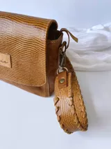 Bandolera color camel de cuero con forro de tela, correa corta con tientos y bolsillo interno.