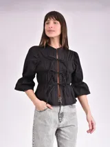Blusa negra con escote mao y mangas 3/4 con volantes. Presenta detalle de frunces en el frente y lazos para ajustar.