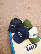 Gorra de gabardina color crudo con visera curva y logo de la marca bordado en negro en el frente.