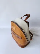 Mochila pequeña de cuero color camel, con base marrón, laterales color crema y cierre superior con cremallera.