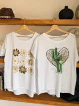 Remera blanca de algodón con cuello redondo y estampado de cerezas rojas con hojas verdes y texto dorado.