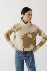 Sweater de punto color beige con cuello alto, diseño con manchas marrones y detalles de costuras rojas.