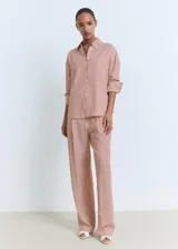 Camisa de manga larga con cuello camisero y cierre frontal de botones. Diseño recto con estampado de rayas verticales en tonos rojizos y beige.