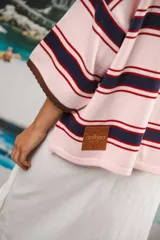 Remera de algodón y poliéster a rayas horizontales rojas y azul marino sobre fondo crudo. Tiene cuello tipo polo con botones, mangas amplias y corte oversized.