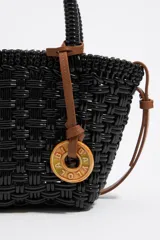 Bolso tipo tote de mimbre color marrón oscuro, con doble asa corta y correa de cuero marrón. Incluye dije circular dorado con letras grabadas.