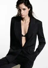 Blazer negro con pequeños apliques brillantes, cuello con solapa, cierre con un botón, dos bolsillos delanteros con solapa, forro interior y corte recto.