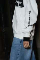 Campera con capucha blanca con cierre frontal y bolsillos tipo canguro. Estampado frontal con logo de Corvette, el año 2005 y la leyenda "Grand Sport". Estampado en la manga con la palabra "Corvette".