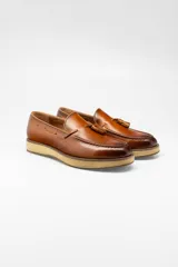 Mocasines de cuero color marrón con borlas decorativas y suela de goma color beige.