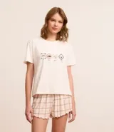 Conjunto de pijama corto compuesto por una remera de algodón blanca con estampado de mascotas y un short de viscosa a cuadros en tonos rosa y beige con volados en el ruedo.