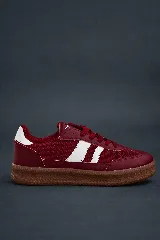 Championes deportivos de mujer color bordó con detalles en blanco. Presentan tres franjas blancas laterales y un parche blanco en el talón. La capellada combina material textil de red y recortes de cuero sintético. La suela es de goma color marrón caramelo.