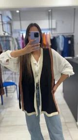 Chaleco largo negro con ribetes marrones y blancos, sin mangas y con lazo para atar en la cintura.