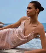 Vestido midi de malla con lentejuelas plateadas, escote recto y tirantes finos cruzados en la espalda. Presenta un forro corto que deja ver la transparencia de la malla con lentejuelas en la parte inferior, creando un bajo asimétrico.