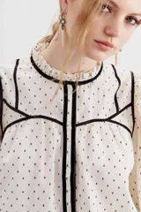 Camisa cruda de algodón con calce relajado y cuello redondo. Detalles de velvet negro y broderie en escote, puños y ruedo.