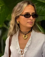 Collar con dije dorado irregular con agujero central, colgando de cordón negro ajustable.