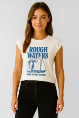 Remera color crema de algodón con estampado de un velero y la frase "Rough Waters Make The Best Sailors" en azul.