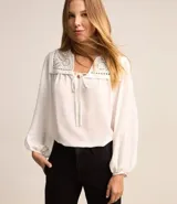 Blusa blanca amplia de viscosa, con lazo delantero, mangas largas abullonadas y canesú con encaje richelieu.