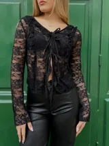 Blusa corta de encaje negro con escote en V, mangas largas acampanadas y lazos ajustables en el frente.