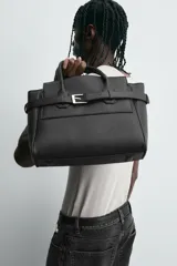 Bolso bandolera negro con detalle de cinturón, compartimento principal con cierre mediante doble imán, bolsillo interior con cierre mediante cremallera, dos asas de mano y un asa de hombro ajustable y extraíble.