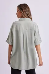 Camisa verde de corte holgado, con cuello clásico, cierre frontal con botones y mangas cortas con dobladillo.