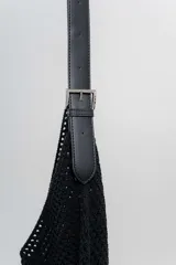 Bolso tejido color crudo con textura calada y correa de eco-cuero negra regulable con hebilla metálica.