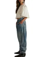 Jean de algodón, color celeste lavado, con tiro alto, pliegues frontales y corte holgado que se estrecha ligeramente hacia el tobillo.