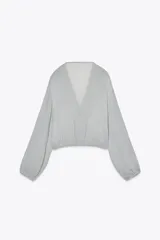 Blusa color marrón con escote en pico, manga larga abullonada con elástico en los puños y volantes en el escote y mangas.