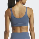 Sostén deportivo Reebok Active Collective DreamBlend color azul grisáceo, con escote en V y breteles anchos. Logo de la marca estampado en el frente.