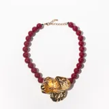 Collar de cuentas color borgoña con dije dorado en forma de flor.
