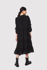 Vestido midi negro con escote en V, mangas largas con volados en los hombros, cintura con lazo ajustable y falda escalonada con volados.