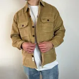 Sobrecamisa color crema de pana con cuello clásico, cierre frontal con botones negros, dos bolsillos de parche en el pecho con solapa abotonada y puños abotonados.