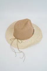 Sombrero de paja de ala ancha, con copa estilo fedora en color marrón y ala en color beige claro con hilos dorados entretejidos. Presenta una cinta decorativa con cuentas turquesas y un lazo de cordón fino atado alrededor de la base de la copa.