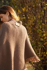 Poncho tejido en lana merino color crudo, con cuello alto y etiqueta de cuero con logo en la espalda.