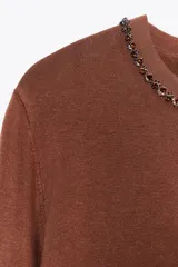 Chaqueta marrón de punto con cuello redondo decorado con abalorios tipo joya y manga larga. Cierre frontal con botones.